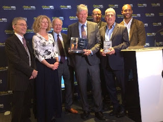 William Finnegan  (centre) shows off the 2016 William Hill  Sports Book of the Year Award, flanked by (left-to-right)  judges Graham Sharpe, Alyson Rudd, Hugh McIlvanney, Mark Lawson, John Inverdale and Clarke Carlisle.