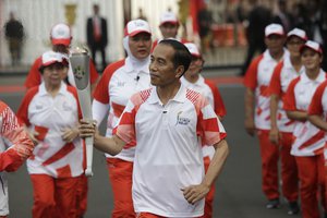 Indonesian President JJoko "Jokowi" Widodo, center, holds the Asian Games torch as he runs during an independence day ceremony at Merdeka Palace in Jakarta, Indonesia, Friday, Aug. 17, 2018