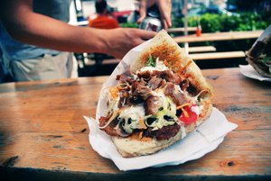 File - A Doner kebab, Cologne, Germany. A Doner kebab is made of meat cooked on a vertical rotisserie and often served with salad or vegetables, which may include tomato, lettuce, cabbage or onion.