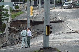 Men stand on an earthquake-damaged street in Kiyota, outskirts of Sapporo city, Hokkaido, northern Japan, Friday, Sept. 7, 2018.