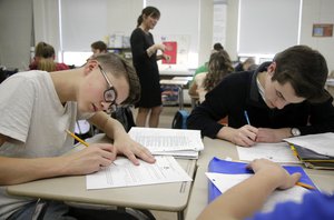 In this Wednesday, March 8, 2017 photo, high school students Jackson Laferriere, left, and Noah Lemoine fill out work sheets as teacher Natalie O'Brien, top center, speaks with students during a civics class