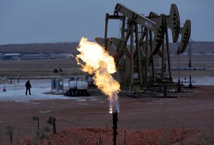 In this Oct. 22, 2015 file photo, workers tend to oil pump jacks behind a natural gas flare near Watford City, N.D.