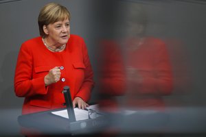 In this photo taken with a reflection in a window of the visitors tribune, German Chancellor Angela Merkel delivers her speech during a plenary session of the German parliament Bundestag about the budget 2019, in Berlin, Wednesday, Sept. 12, 2018.