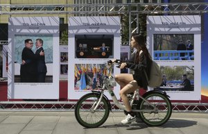 A woman rides a bicycle to pass by photos of the summit between South Korean President Moon Jae-in and North Korean leader Kim Jong Un during a photo exhibition to celebrate the upcoming inter-Korean summit in Seoul, South Korea, Monday, Sept. 17, 2018. A senior South Korean official is playing down the chance that this week's inter-Korean summit could produce major progress in efforts to rid North Korea of its nuclear program. (AP Photo/Ahn Young-joon)