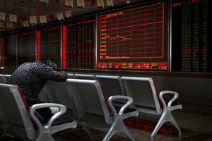 An investor takes a nap in front of an electronic board displaying stock prices at a brokerage house in Beijing, Monday, Sept. 17, 2018.