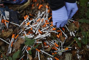 In this Nov. 8, 2017, file photo, a volunteer cleans up needles used for drug injection that were found at a homeless encampment in Everett, Wash.