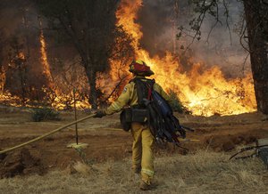 A firefighter walks to flames as a wildfire advances onto a residential district Saturday, July 28, 2018, in Redding, Calif.