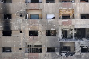 In this Monday, April 16, 2018 photo, people look out of their damage apartment windows just meters away from where the alleged chemical weapons attack occurred in the town of Douma, the site of a suspected chemical weapons attack, near Damascus, Syria