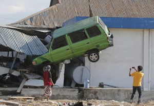 A man takes a photo of a car lifted into the air with his mobile phone following a massive earthquake and tsunami at Talise beach in Palu, Central Sulawesi, Indonesia, Monday, Oct. 1, 2018.