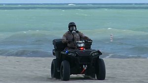 In this image made from video, a Miami-Dade police officer is seen wearing a gas mask and riding an ATV in Miami Beach, Fla., on Thursday. Oct. 4, 2018.