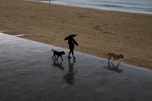 A woman holding a umbrella walks along the beach, during rainfall in Barcelona, Spain, Wednesday, Oct. 10, 2018.