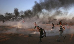 Protester run to take cover from teargas fired by Israeli troops while others burn tires near the fence of the Gaza Strip border with Israel during a protest east of Khan Younis, southern Gaza Strip, Friday, Oct. 12, 2018.