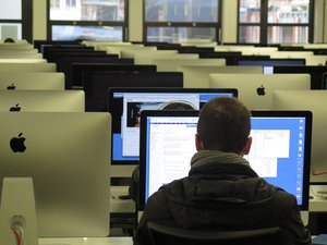 Rear view of man working in office with iMac desktop computers