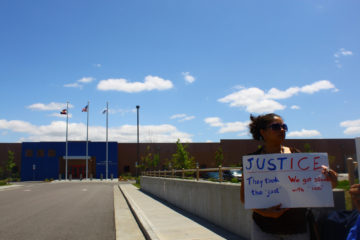 A protester stands with a sign in front of an immigrant detention center in Aurora, Colorado, operated by the private prison company GEO Group. Photo by Justin Valas on Flickr