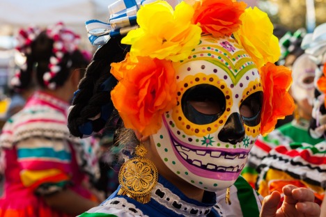 Girl wearing colorful skull mask and paper flowers for Dia de Los Muertos/Day of the Dead celebration