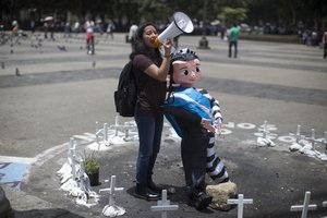 Activist Andrea Ixchiu holds an effigy of Guatemala's President Jimmy Morales and shouts slogans in support of Ivan Velasquez, chief of a U.N. anti-corruption commission, in the middle of an altar honoring dozens of girls who died in a fire at a children's home this year, in the Central Plaza of Guatemala City, Monday, Aug. 28, 2017.