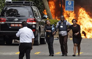 Security forces help civilians flee the scene as cars burn behind, at a hotel complex in Nairobi, Kenya Tuesday, Jan. 15, 2019.