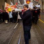 November 5th - March down bay street to protest austerity for the poor, bail outs for the rich. Someone holding a megaphone at the front, protesters behind.