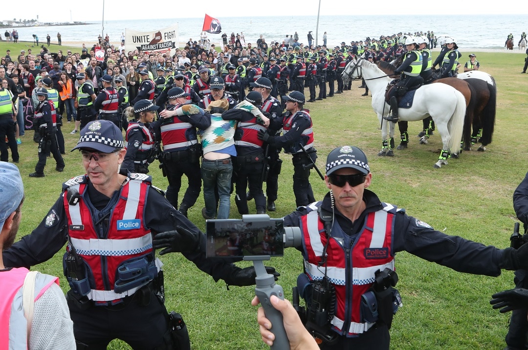 Police keep protesters apart as a man is arrested on the St Kilda foreshore in Melbourne.