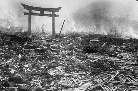 Here is a city street completely reduced to rubble, with fires smoldering in the background and smoke hanging in the air. A single Shinto gateway remains standing over the rubble.