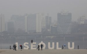 A woman wearing a mask poses as the cityscape is covered with a thick haze of fine particles of dust in Seoul, South Korea, Tuesday, March 5, 2019.