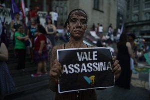 An activists covered in mud poses with a sign that reads "Vale assassin" during a demonstration on the front steps of Sao Paulo's Cathedral, Brazil, Friday, Feb. 1, 2019.  The Brumadinho dam disaster, owned by Vale, killed at least 115 people.