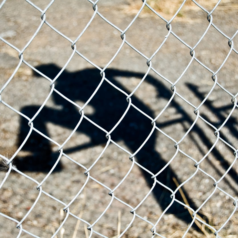 shadow of a person climbing over a barbed-wire fence