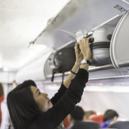 Woman putting cabin carry on bags luggage in plane overhead bin locker