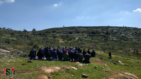 Palestinian demonstrators are kneeling down in prayer on a rocky hill