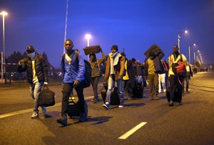 Migrants carrying their belongings leave a makeshift camp known as "the jungle" near Calais, northern France, to register at a processing centre, Monday Oct. 24, 2016.