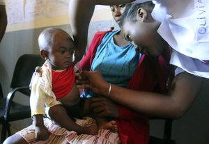 In this photo taken on Thursday, March 21, 2019, a volunteer nurse examines 6-moth-old Sarobidy, who is infected with measles, while her mother Nifaliana Razaijafisoa looks on, at a healthcare centre in Larintsena, Madagascar.