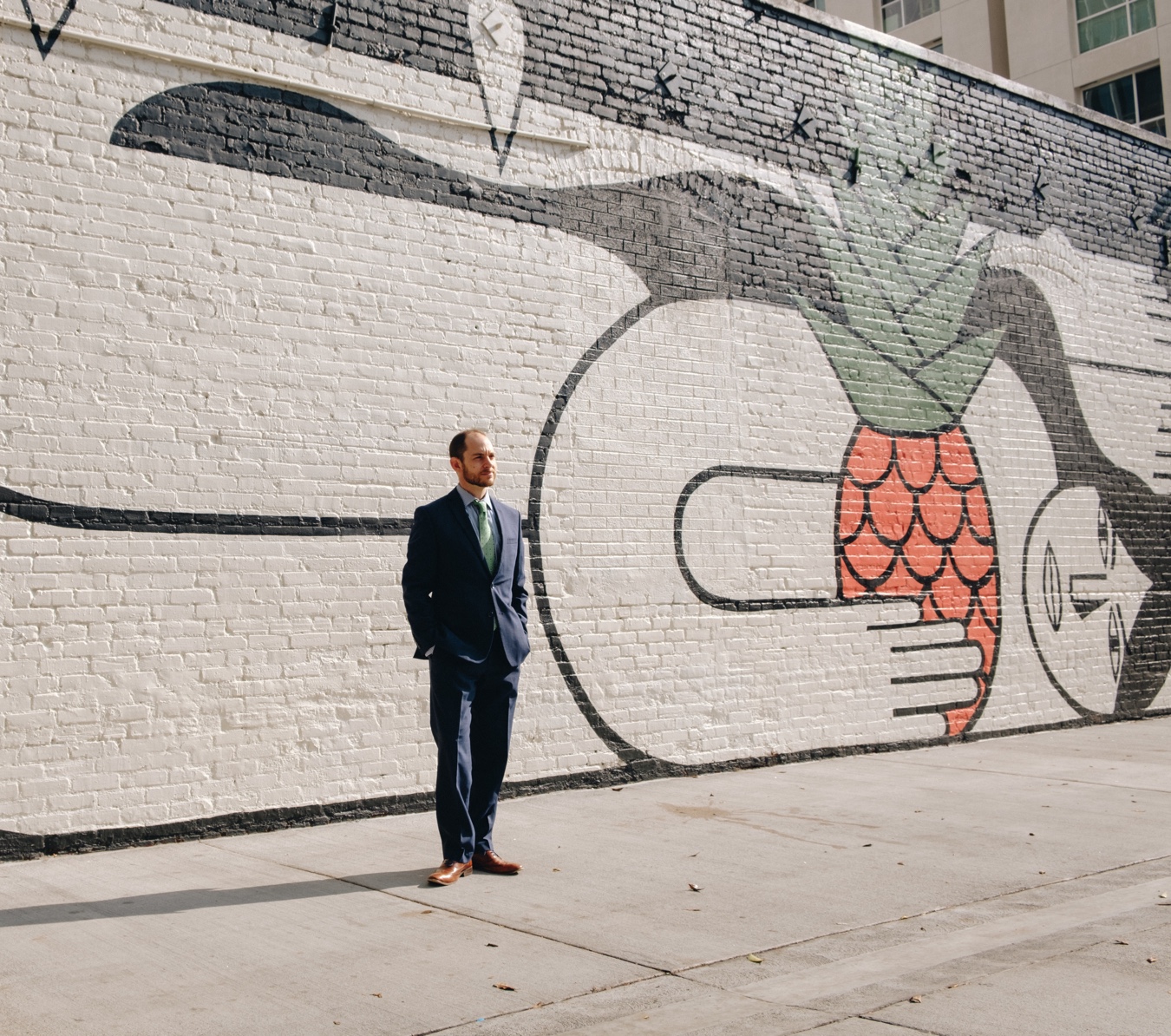 Portrait of Brian Rosenbaum, wearing a suit, standing in front of an enormous and beautiful black and white and pink mural in Downtown Los Angeles.