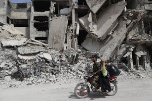 File - A Syrian Soldier rides his scooter as helps a woman to through a devastated part of the in the Palestinian refugee camp of Yarmouk in the Syrian capital Damascus, Syria, Saturday, Oct. 6, 2018.