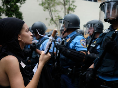 A woman stands in front of a riot police line during a May Day protest against pension cuts, school closures and slow hurricane recovery efforts in San Juan, Puerto Rico, on May 1, 2018.