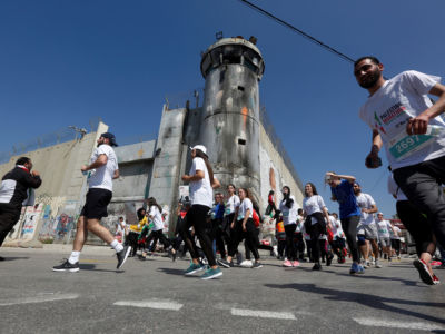 Runners in the Palestine Marathon pass a guard tower and border wall