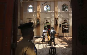 In this Thursday, April 25, 2019 photo, a policeman stands guard, as surveyors work at St. Sebastian's Church, where a suicide bomber blew himself up on Easter Sunday in Negombo, north of Colombo, Sri Lanka