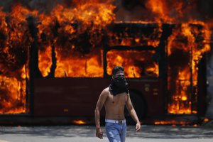 An anti-government protester walks near a bus that was set on fire by opponents of Venezuela's President Nicolas Maduro during clashes between rebel and loyalist soldiers in Caracas, Venezuela, Tuesday, April 30, 2019.