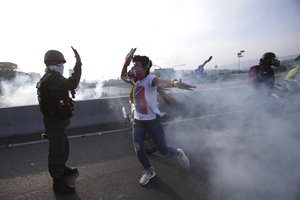 An opponent to Venezuela's President Nicolas Maduro high fives a rebel soldier on a highway overpass outside La Carlota air base amid tear gas fired by loyalist soldiers inside the base in Caracas, Venezuela, Tuesday, April 30, 2019.