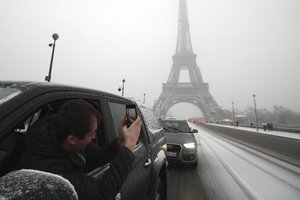 A driver takes a snapshot of the Eiffel Tower during first snowfall of the winter season in Paris, France, Tuesday, Feb. 6, 2018.