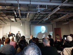 John Pilger, Richard Gizbert, and Julian Assange (on screen) at  The Wikileaks Files  Book Launch, Foyles book shop,  London   29th September, 2015.