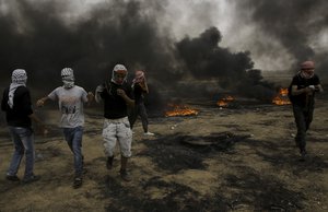 Palestinian protesters run for cover from teargas fired by Israeli troops after they burn tires during a protest at the Gaza Strip's border with Israel, east of Khan Younis, Friday, May 4, 2018.