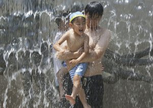 A man holds a child at a water fall to cool off at a park in Tokyo, Monday, July 16, 2018.