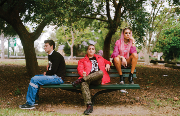 Three people sit on a park bench looking unhappy.