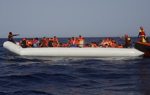 In this Saturday, June 30, 2018 photo, an Open Arms lifeguard gives a thumbs-up to a migrant at the other end of a rubber boat in the middle of a rescue operation some 30 nautical miles off the coast of Libya in the Mediterranean Sea.