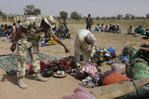 FILE- In this Tuesday, Dec. 8, 2015 file photo, soldiers guard people fleeing from Boko Haram’s carnage and about to be searched to ensure there are no insurgents infiltrating a refugee camp.