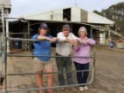 A middle-aged man and woman stand at a farm gate lean on a farm gate at a dairy with a younger woman