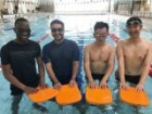 Four young men in the swimming pool with kickboards.