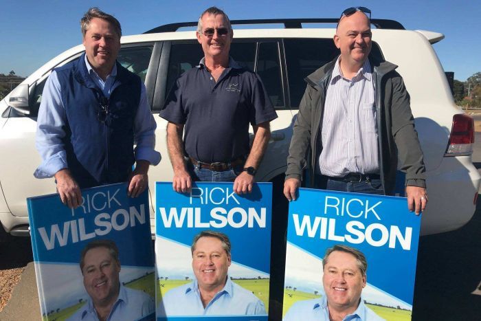 Three Liberal supporters holding up campaign posters.