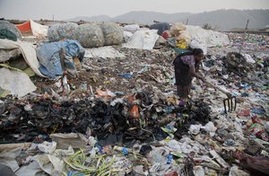 An Indian woman makes a drain for dirty water to pass next to plastic bottles collected for recycling at a garbage dumping site in Gauhati, India, Wednesday, Mar 7, 2018