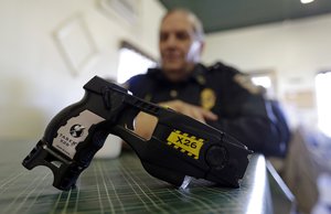 In this Nov. 14, 2013, file photo, a Taser X26 sits on a table in Knightstown, Ind. In the recent shootings of unarmed black men in a San Diego suburb and in Tulsa, Oklahoma, the police officers who fired the fatal shots were accompanied by officers who simultaneously drew their stun guns.